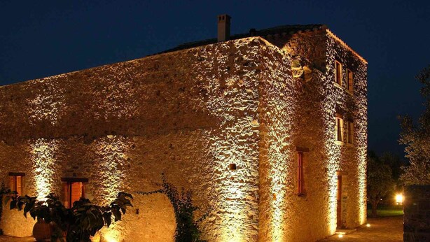 A stone building with illuminated walls and a table set for dining outdoors at night. - Liotrivi Historical Mansion & Hotel (Monemvasia)