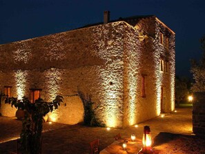 Un edificio de piedra con paredes iluminadas y una mesa dispuesta para cenar al aire libre por la noche.