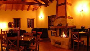 A cozy living room with a fireplace, wooden furniture, and a high ceiling. - Liotrivi Historical Mansion & Hotel (Monemvasia)