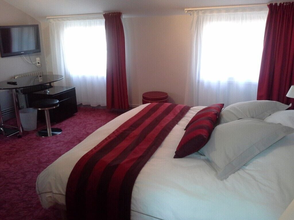 Une chambre d’hôtel avec un lit, un bureau, une chaise, une télévision et une fenêtre avec des rideaux.