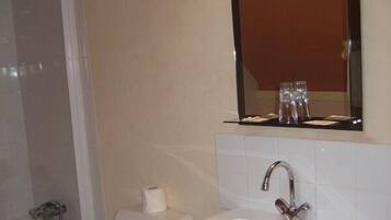 Un baño con inodoro blanco, lavamanos con espejo y zona de ducha.