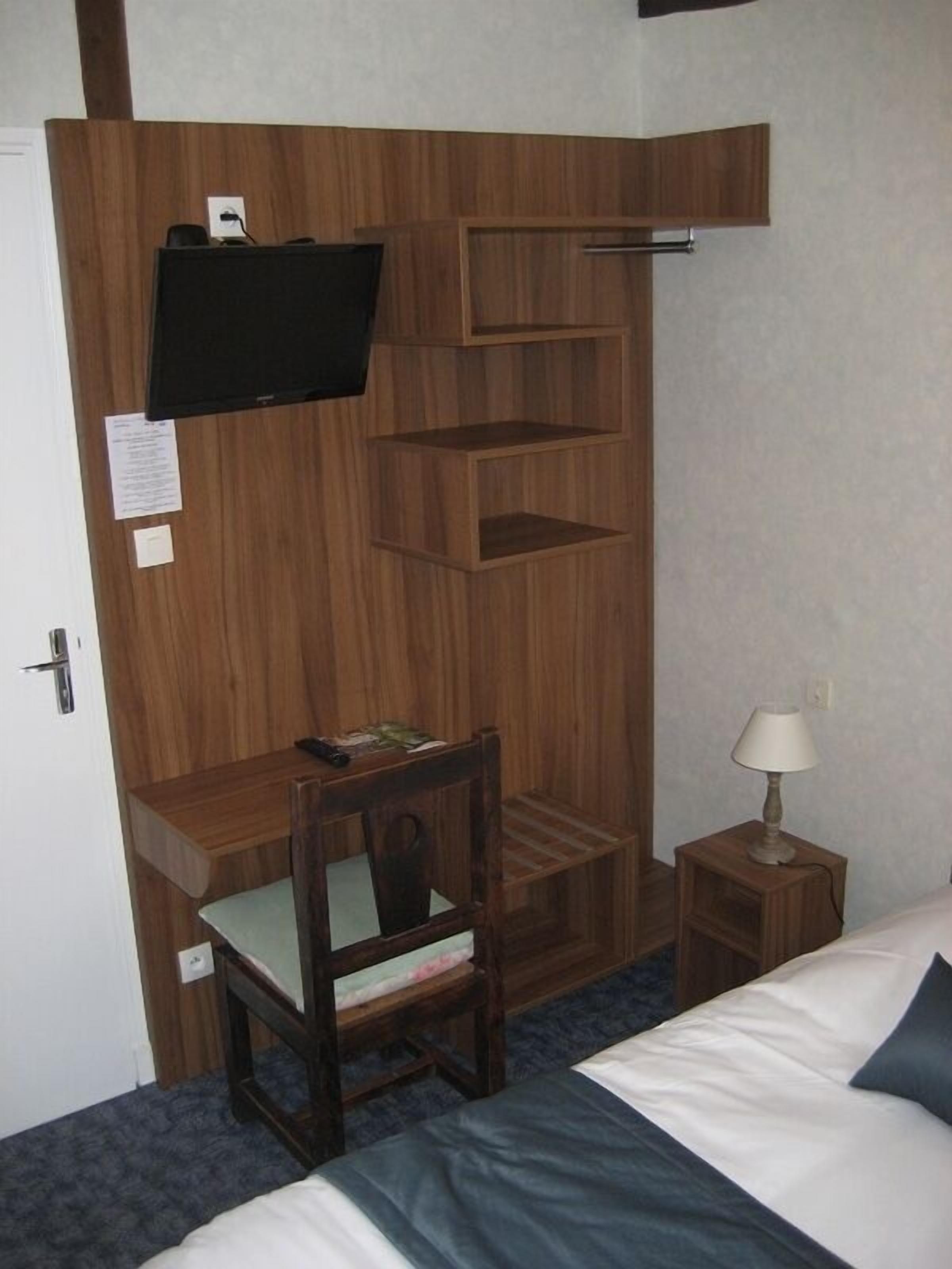 Ein kleines Hotelzimmer mit Holztisch, Stuhl, Bett und Nachttisch mit Lampe.