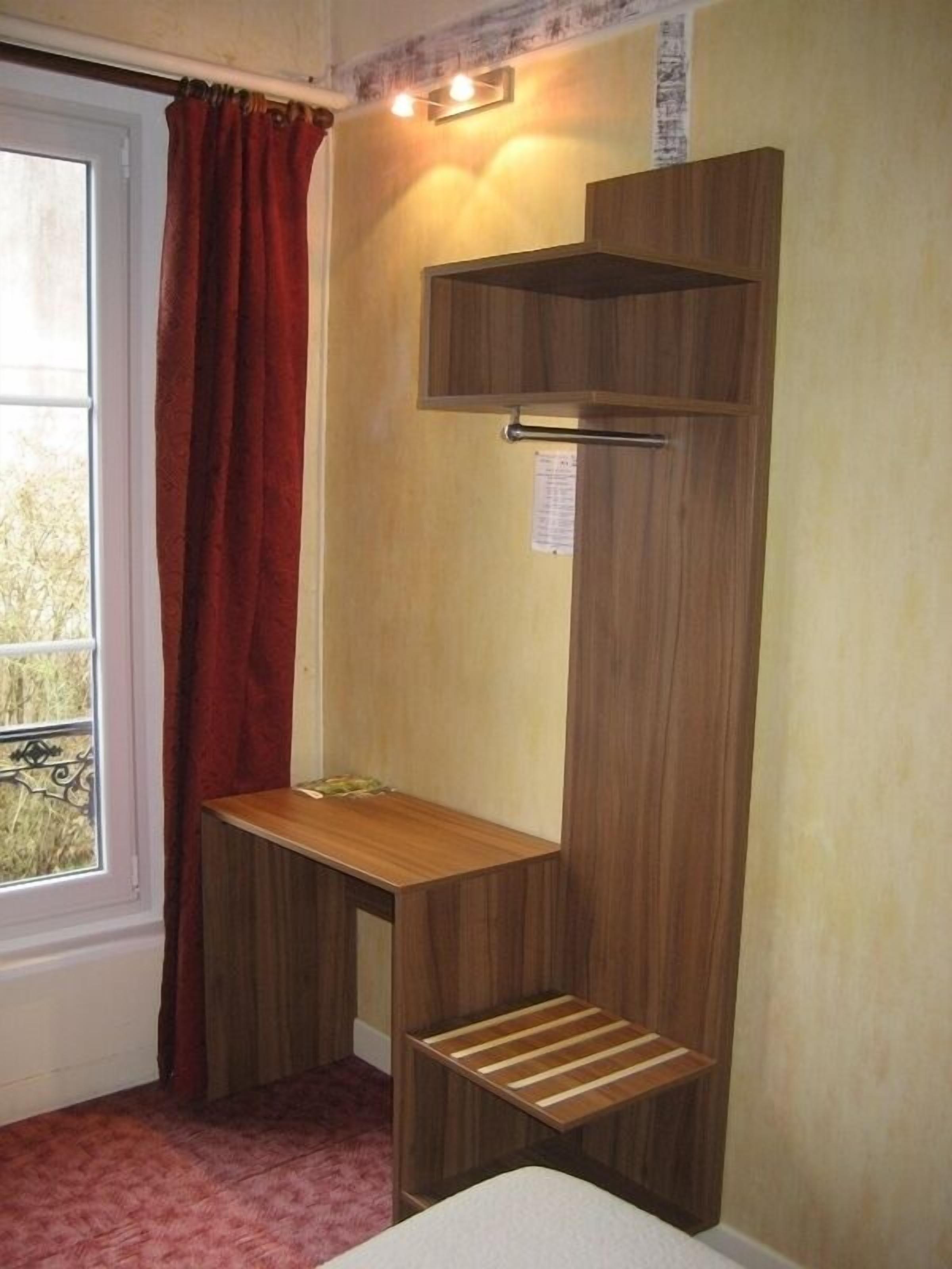 A corner room with a wooden desk, a small shelf, and a window with a red curtain.