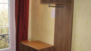 A corner room with a wooden desk, a small shelf, and a window with a red curtain.