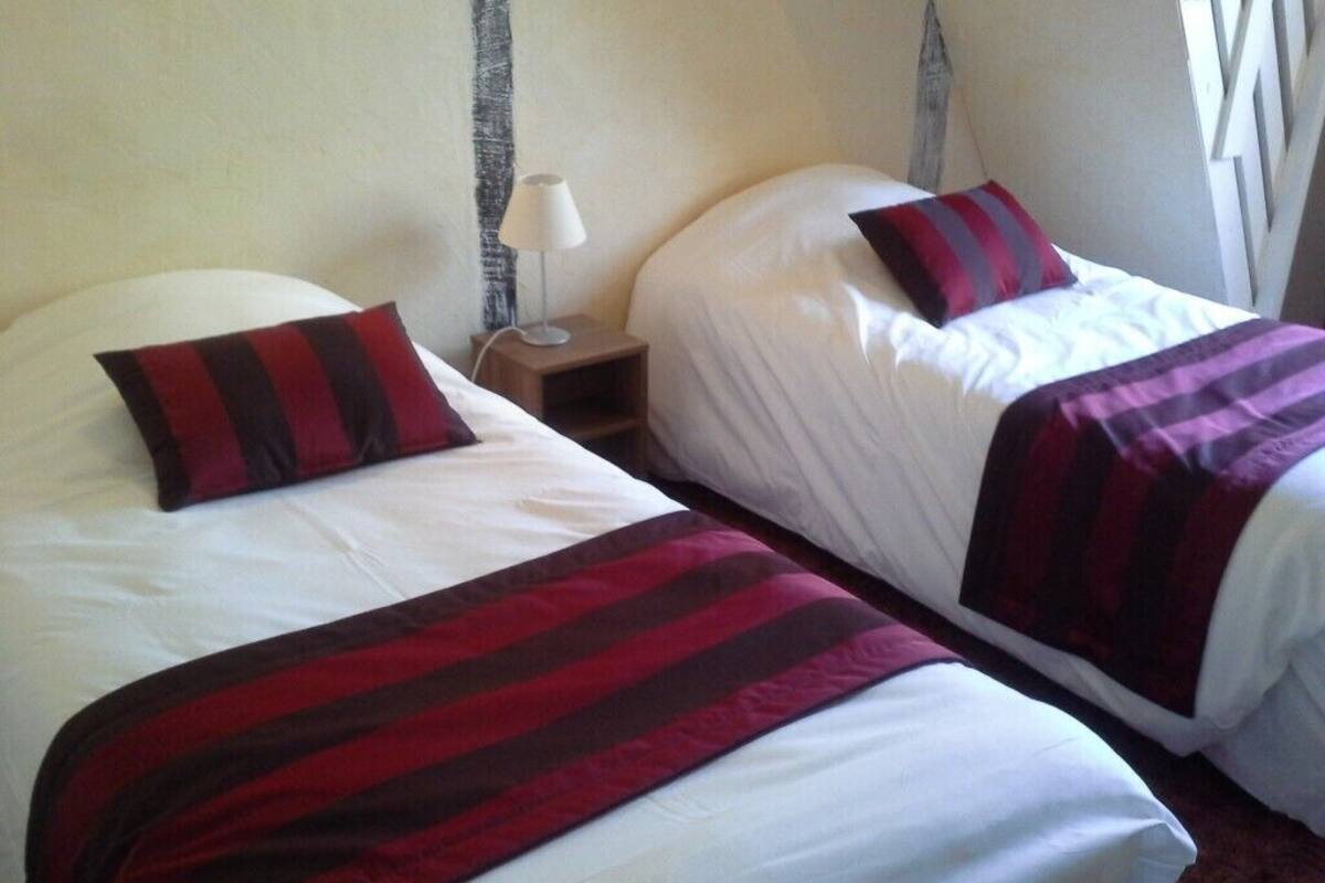Deux lits simples avec des couvertures rayées rouges et noires, une table de chevet avec une lampe et une fenêtre avec des rideaux.