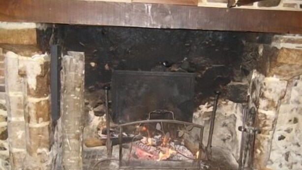 A fireplace with a metal grate and burning logs, set in a stone wall with a brick base.