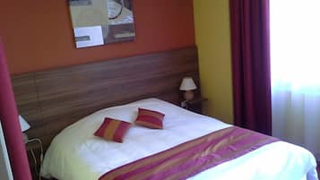 Una cama bien hecha con una colcha blanca y dos almohadas, un cabecero de madera, una mesita de noche con una lámpara y una obra de arte en la pared.