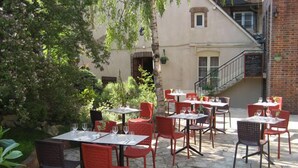 An outdoor patio with stone flooring, red and black chairs, and tables set for dining.