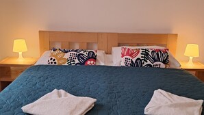 A neatly made bed with a blue quilt, two white towels, and patterned pillows. There are two bedside lamps with yellow shades. - Hotel Garni Rambousek (Prague)