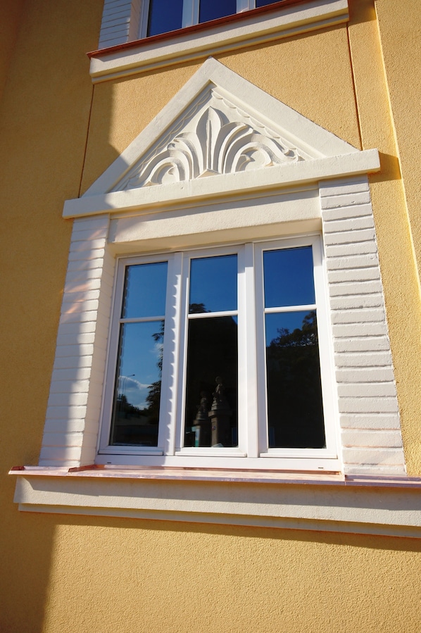 Une fenêtre dotée d’un cadre décoratif blanc et d’un fronton triangulaire.