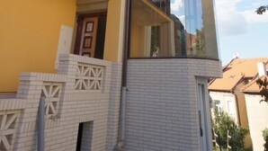 A corner of a building with a yellow facade, a balcony with a black railing, and a glass extension. - Hotel Garni Rambousek (Prague)