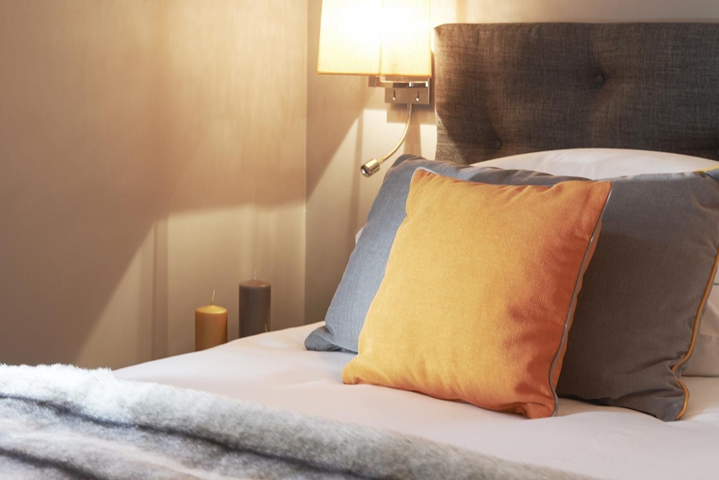 Una cama bien hecha con una colcha blanca y tres almohadas en tonos de azul, amarillo y gris.