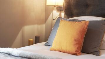 Una cama bien hecha con una colcha blanca y tres almohadas en tonos de azul, amarillo y gris.