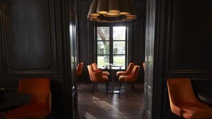 A dining area with a wooden herringbone floor, dark paneled walls, and orange upholstered chairs around a central table. - Maison d'Anthouard (Ecully)