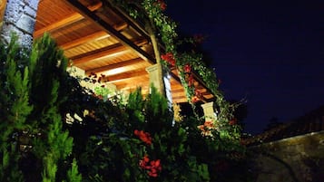 Un edificio con techo de madera y paredes de piedra, rodeado de abundante vegetación y plantas con flores.