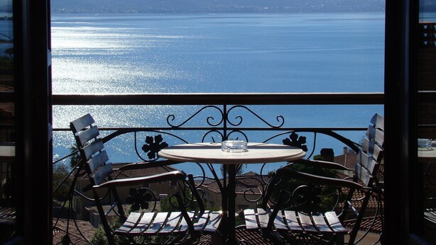 Un balcón con mesa y sillas con vistas a un cuerpo de agua y montañas.