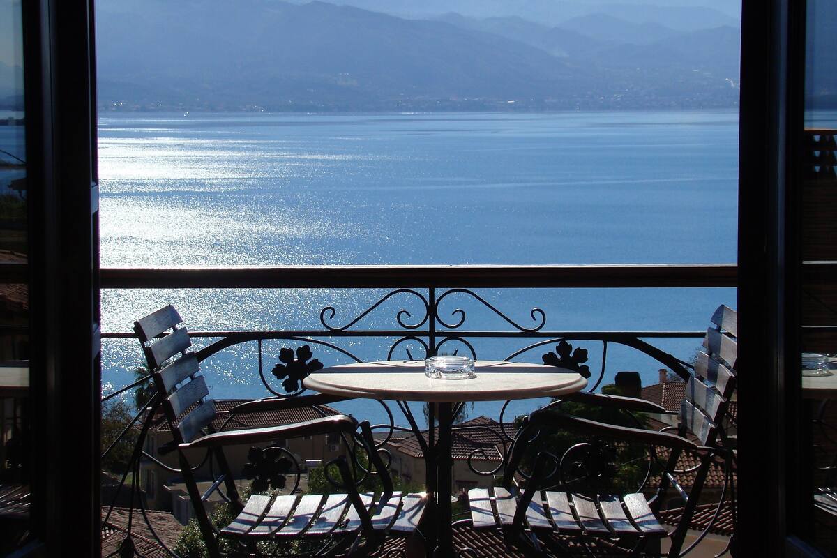Ein Balkon mit Tisch und Stühlen mit Blick auf ein Gewässer und Berge.