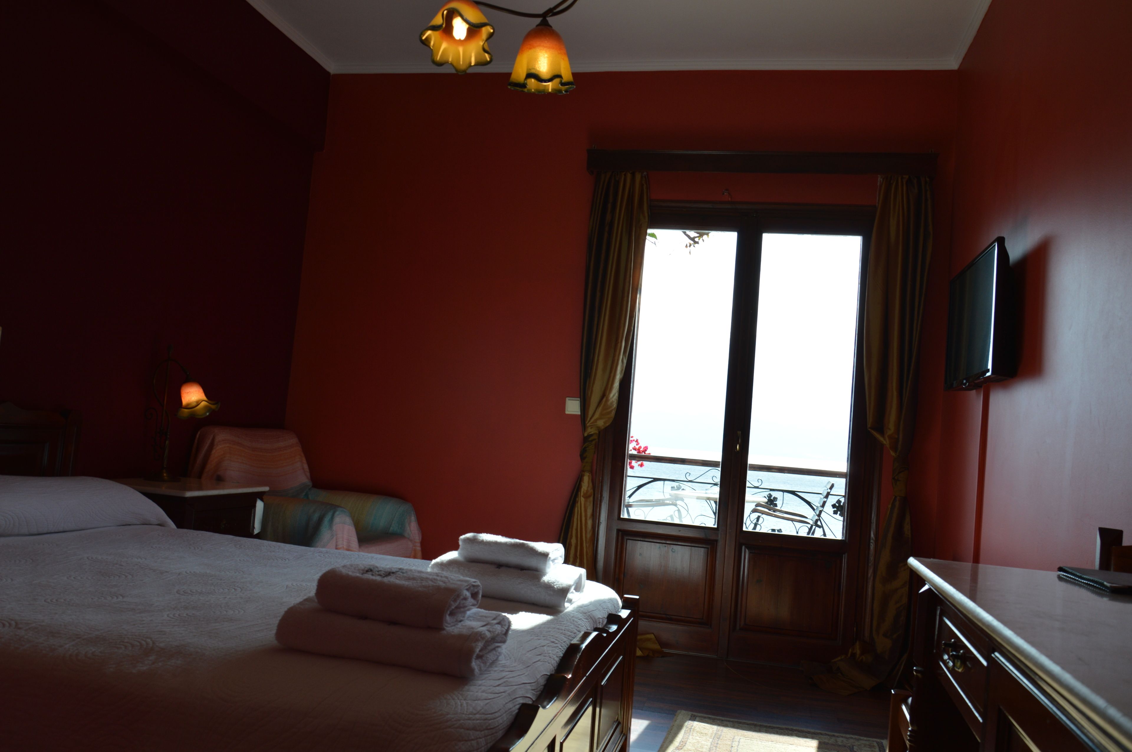 A hotel room with a bed, a desk, a chair, a TV, and a window with a view of a balcony.