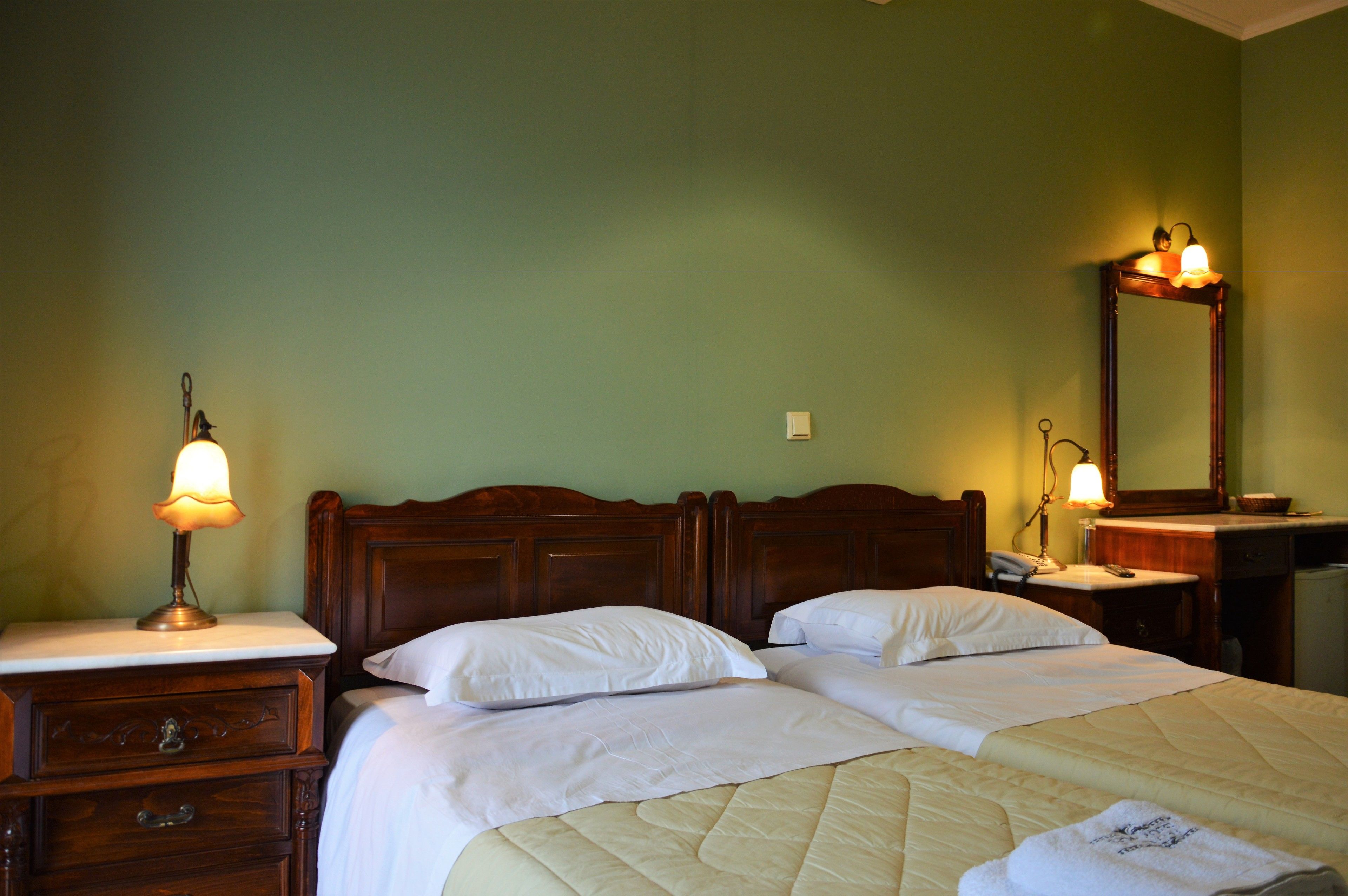 A hotel room with a double bed, two bedside tables with lamps, a wooden dresser, a mirror, and a small desk with a telephone.