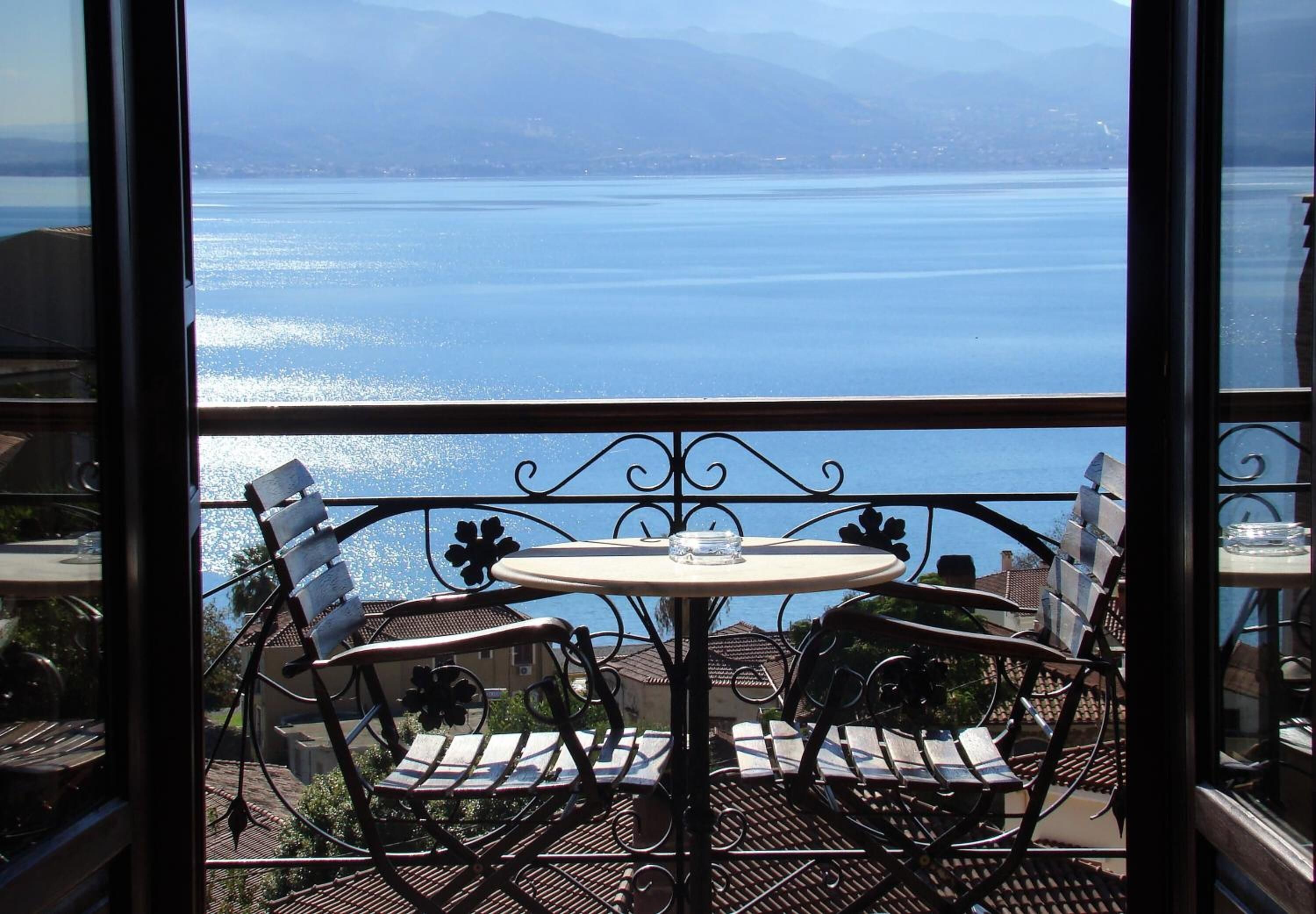 A balcony with a table and chairs overlooking a body of water and mountains.