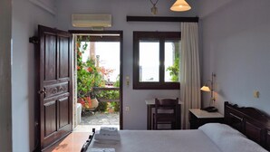 Habitación de hotel con cama, escritorio, silla, ventana con cortinas, aire acondicionado y vistas al balcón exterior con plantas.