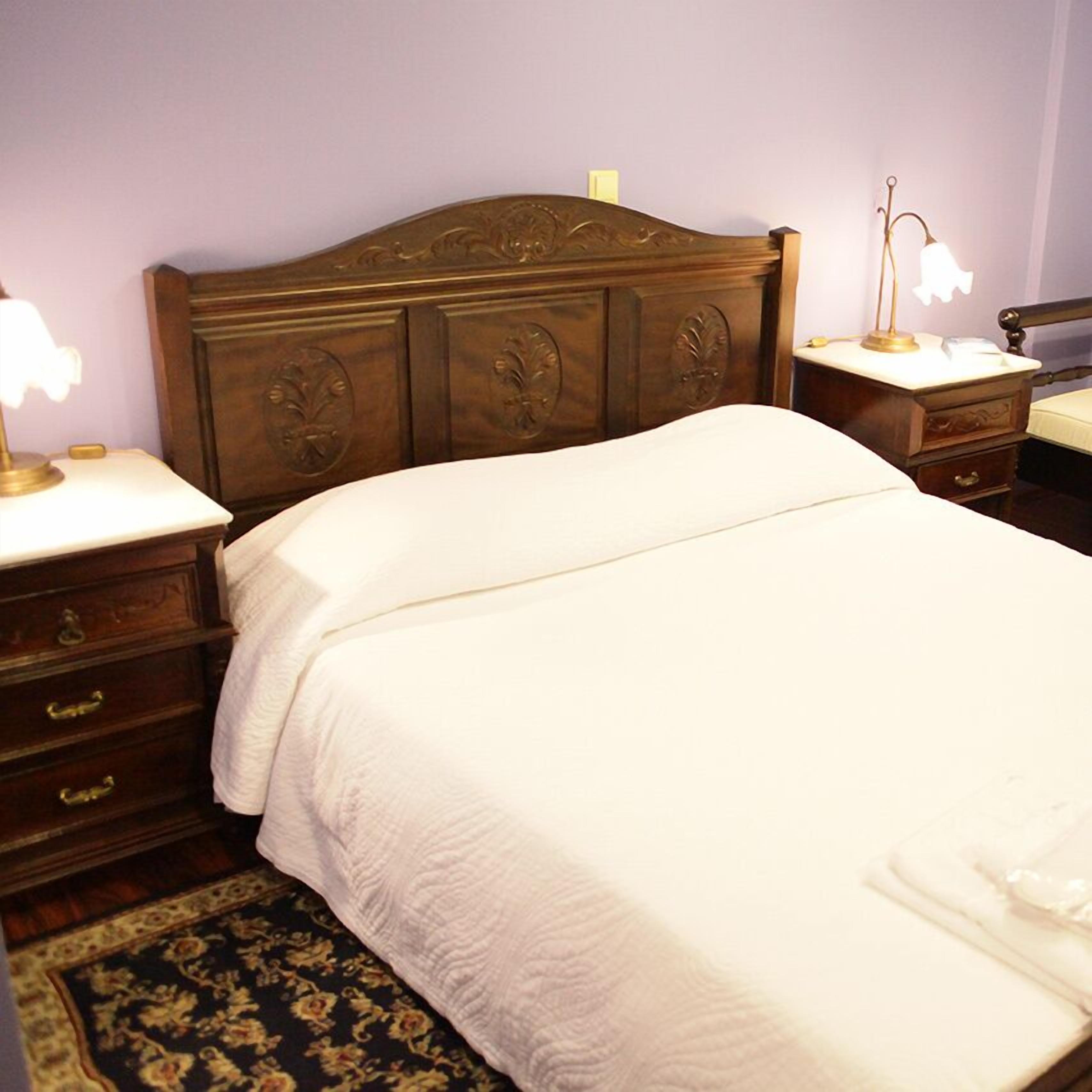 A neatly made bed with a wooden headboard, two bedside tables with lamps, and a patterned rug on the floor.
