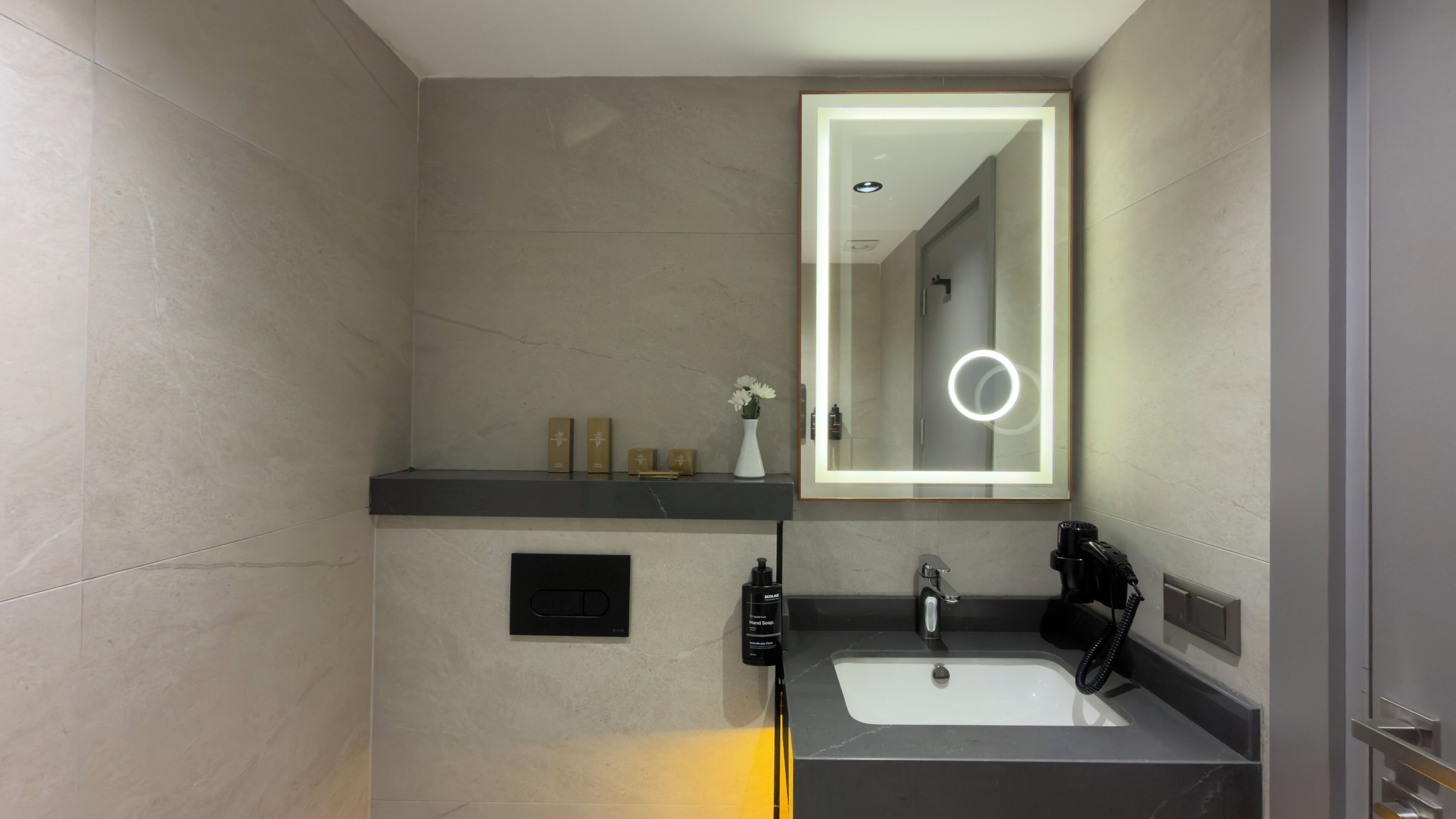 A modern bathroom with a large mirror, a black countertop, a white sink, and a black handheld showerhead.
