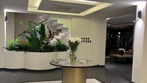A modern lobby with a round table, potted plants, and a staircase. - Göcek Lykia Resort Hotel (Fethiye)
