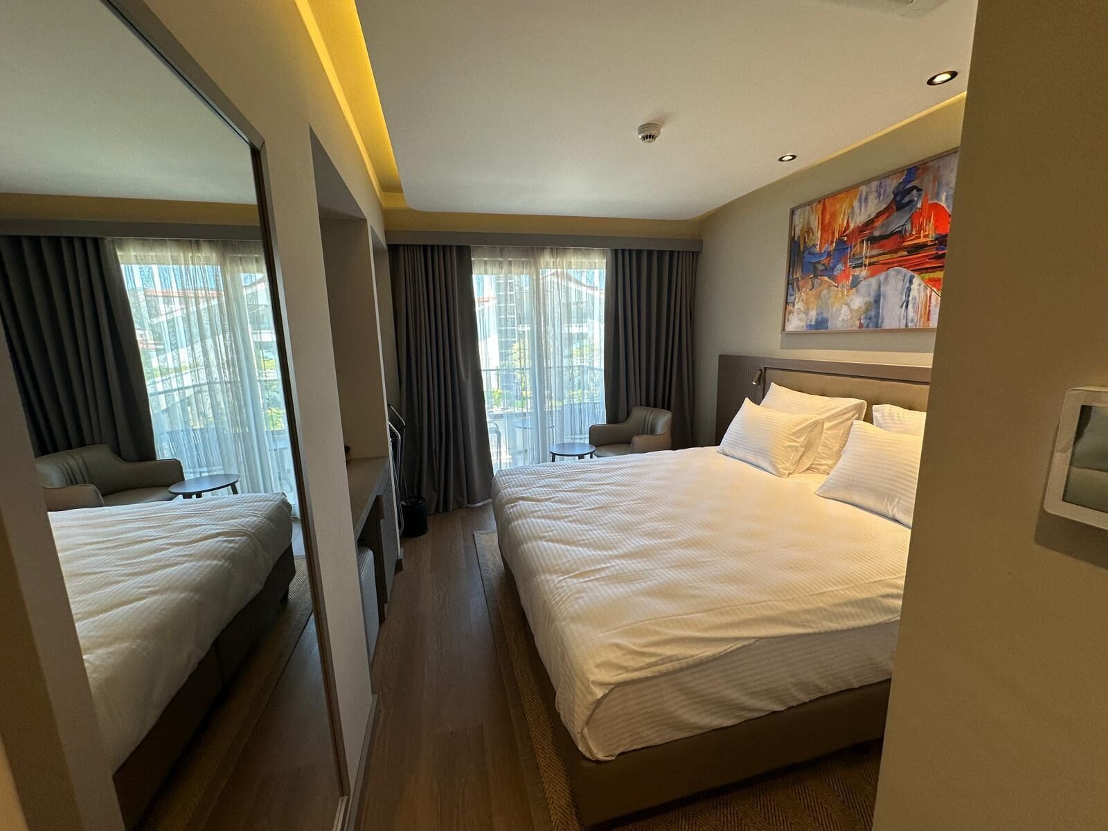 Habitación de hotel con dos camas, un espejo grande, un cuadro y vistas al exterior.