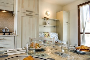 A compact kitchen with white cabinetry, a dining table with a floral tablecloth, and a sofa in the background.