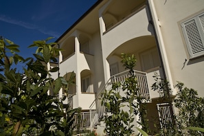A two-story building with a white facade, multiple balconies, and a staircase leading to the upper floor.