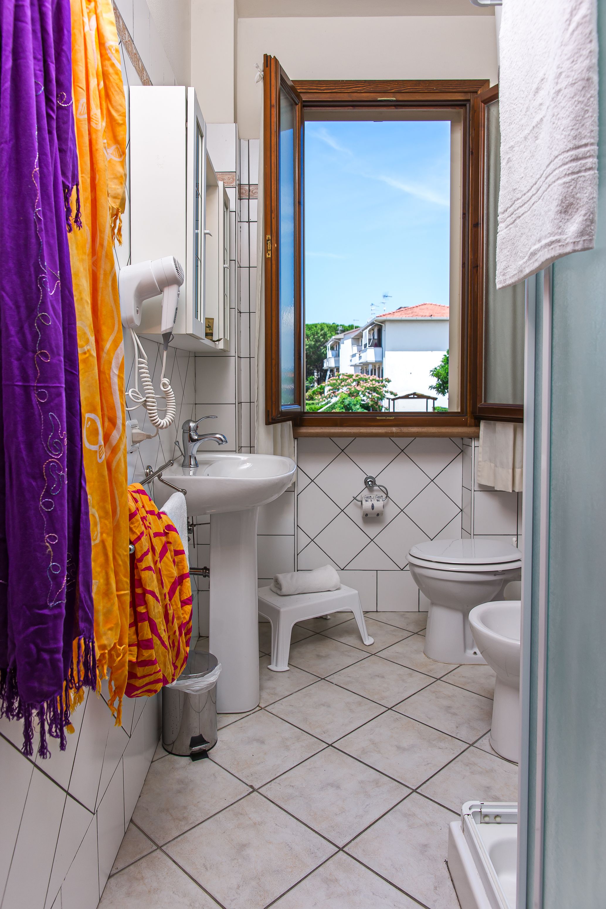 Un baño con ventana, lavamanos blanco, inodoro y bañera.