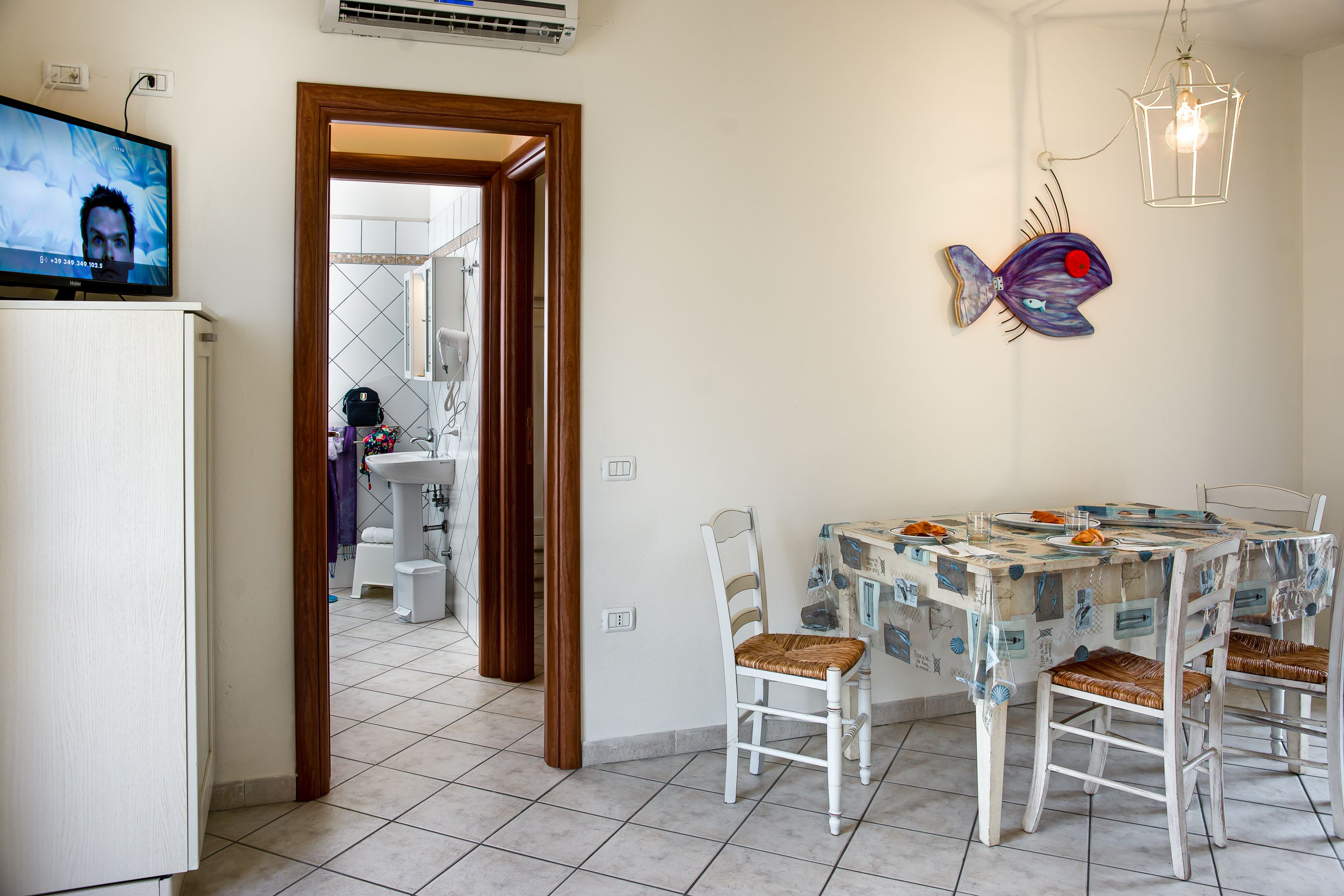 Un comedor con una mesa dispuesta para cuatro personas, sillas blancas y un tapiz decorativo con peces.