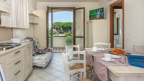 Une cuisine avec un coin repas, une vue sur le jardin et un téléviseur fixé au mur.