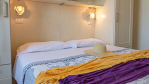 Un lit bien fait, avec des draps blancs, un chapeau tressé et une couverture colorée.