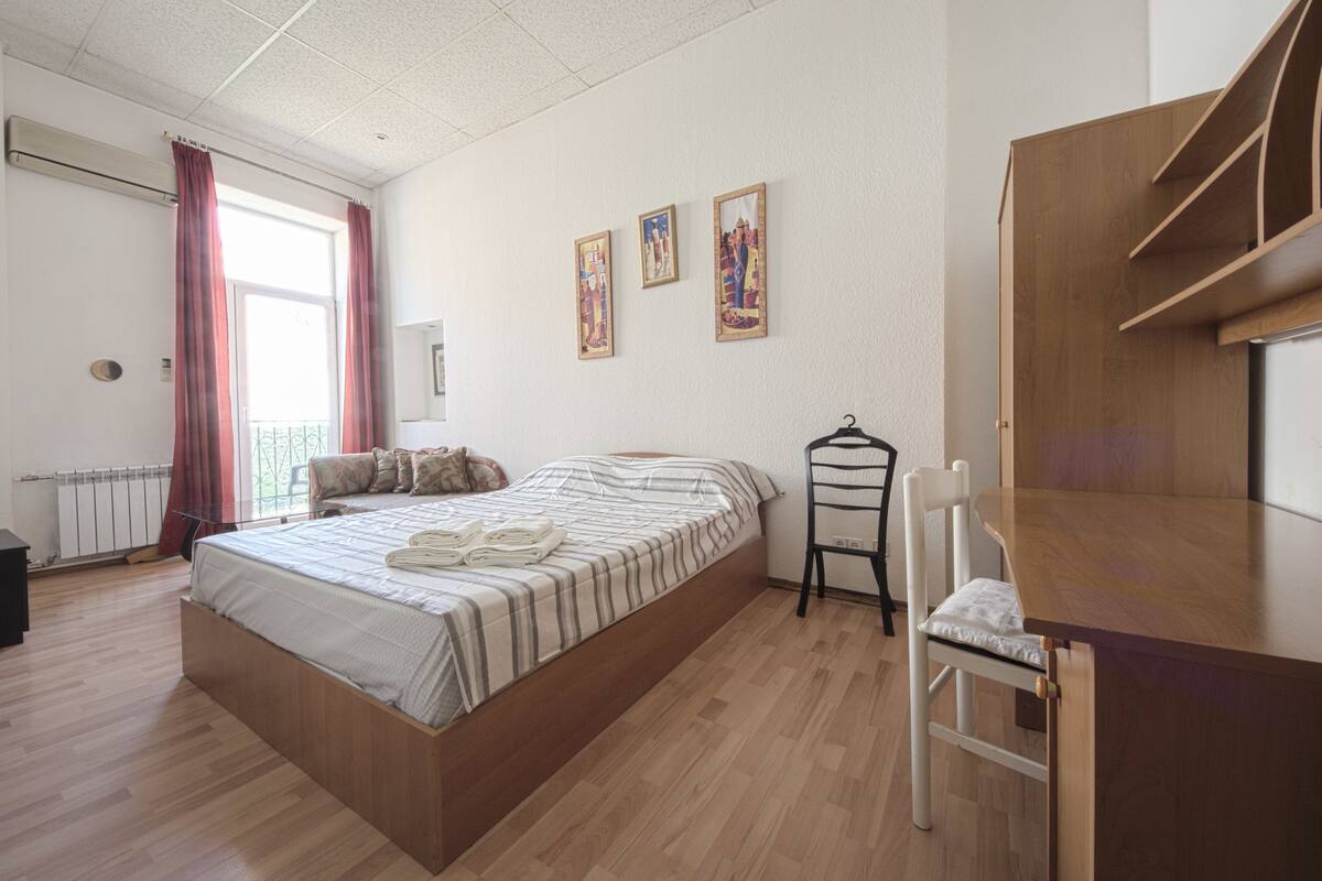 Un dormitorio con una cama de madera, un escritorio pequeño y una silla. Hay tres cuadros en la pared.