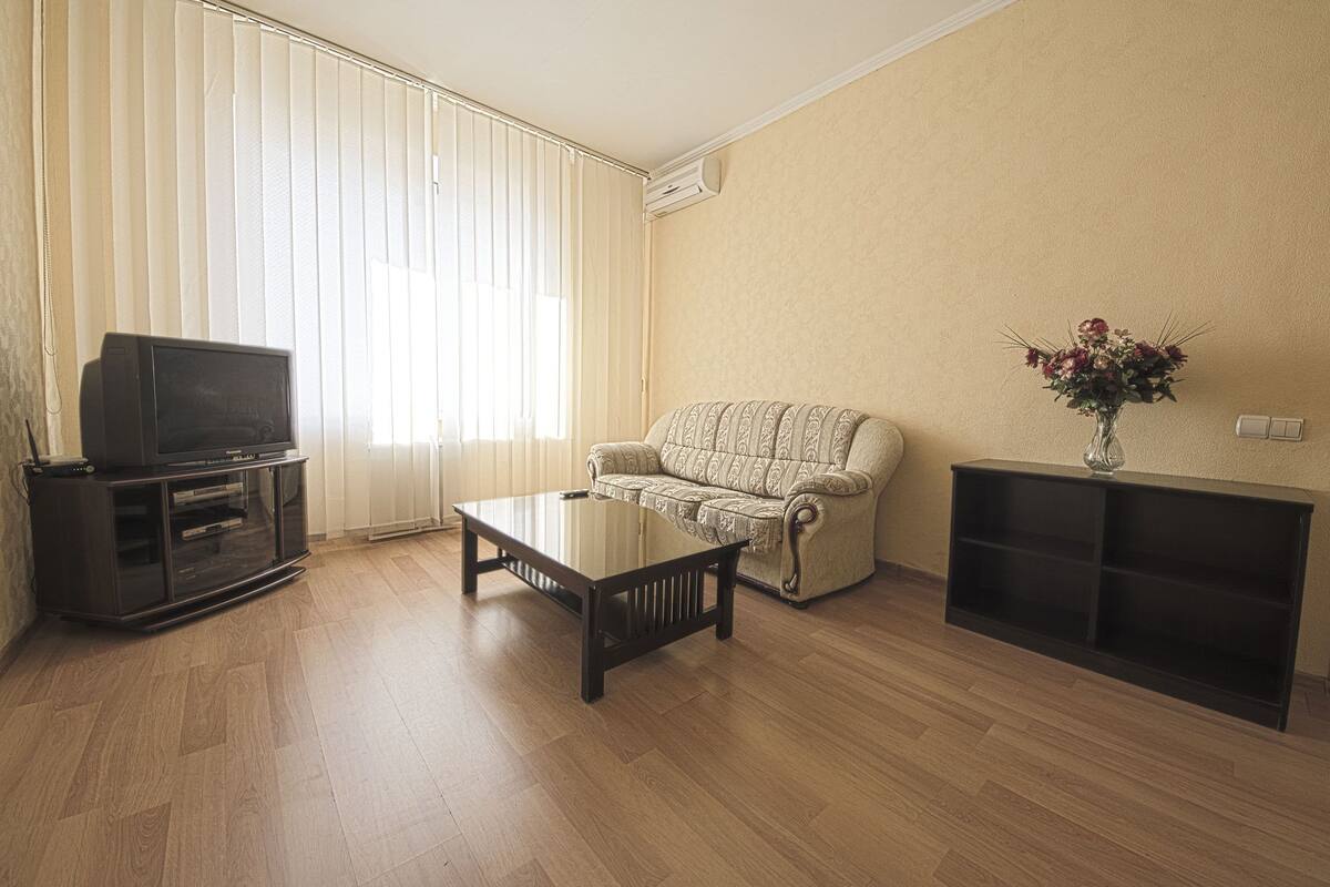 Una sala de estar con sofá, mesa de centro, mueble para televisión y una planta.