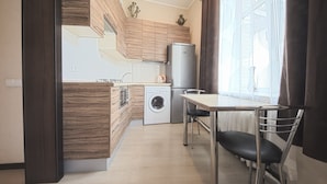 A modern kitchen with wooden cabinets, a washing machine, and a dining area with a table and chairs.