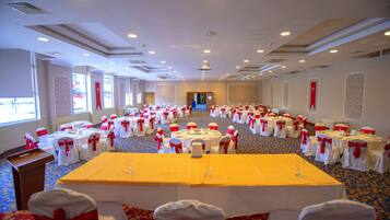 Un salón de banquetes con mesas redondas y sillas, cada una con cintas rojas, dispuestas en filas.