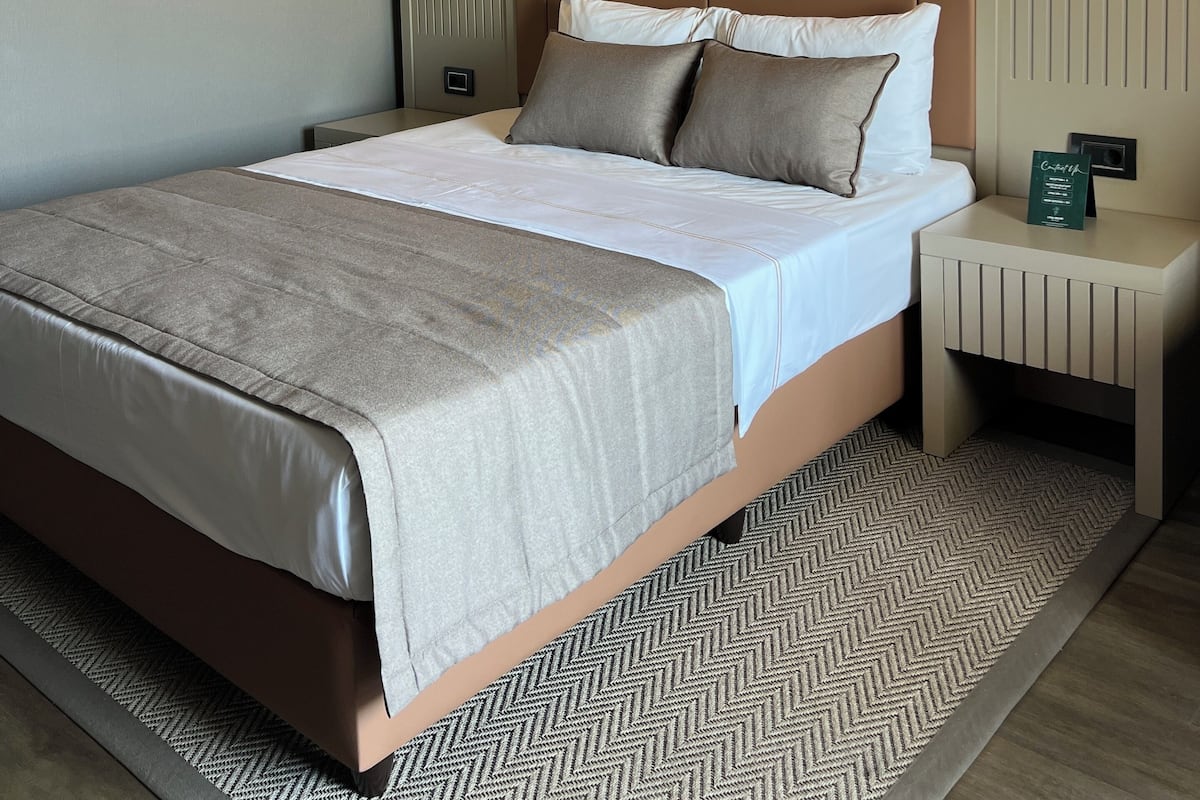 A modern hotel room with a large bed, a nightstand, a wall-mounted light, and a decorative item on the nightstand.