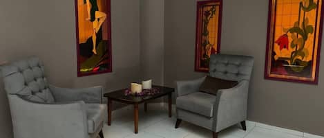 A room with two grey armchairs, a small table with candles, and two framed artworks on the walls.