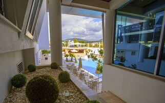 Zona junto a la piscina con vistas a la montaña, mobiliario exterior y un edificio con fachada de vidrio.