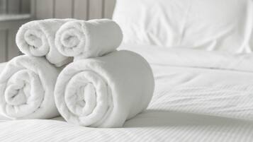 A neatly made bed with rolled white towels stacked on top.