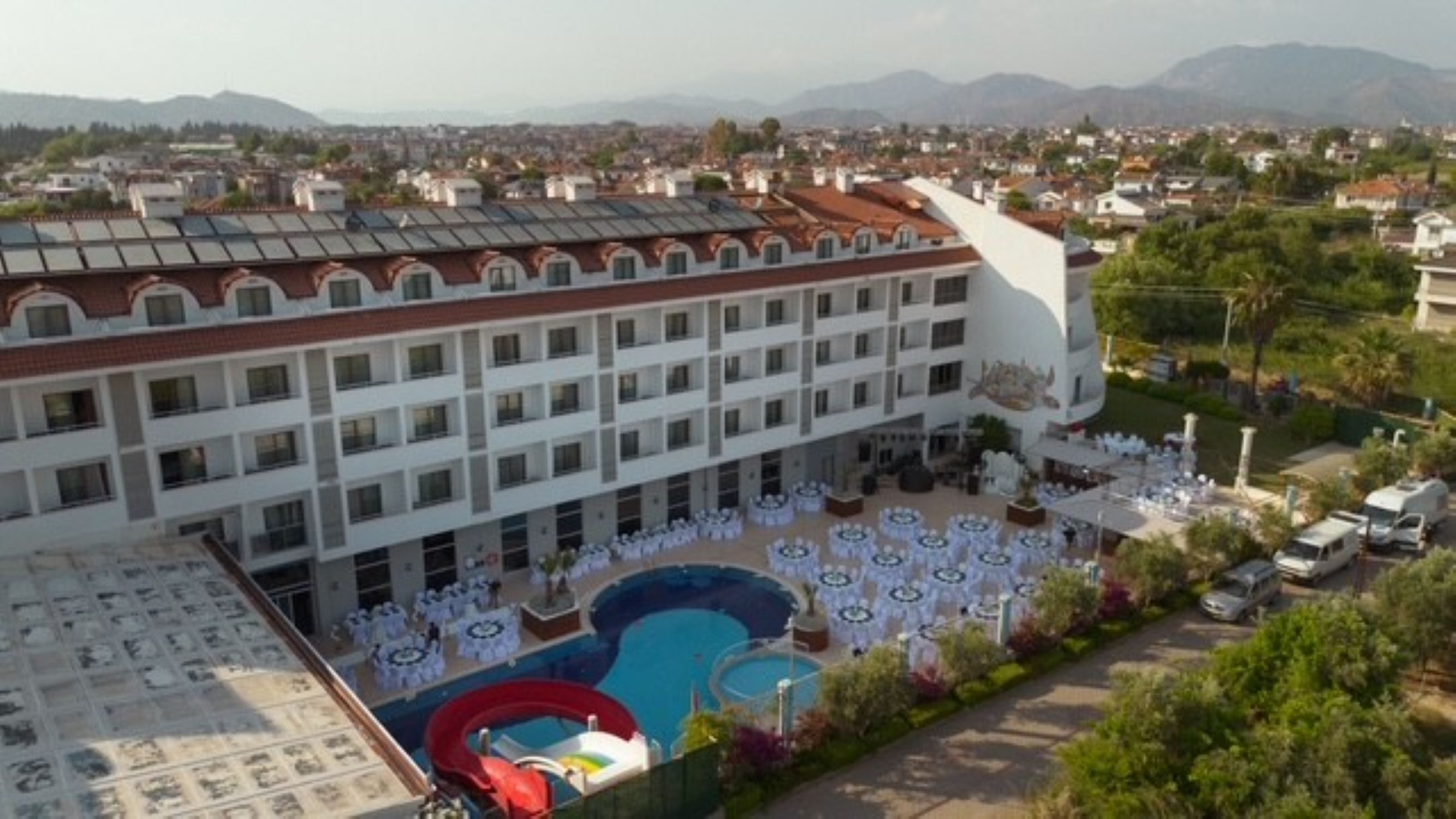 A hotel with multiple floors, outdoor pool area, and a large building in the background.