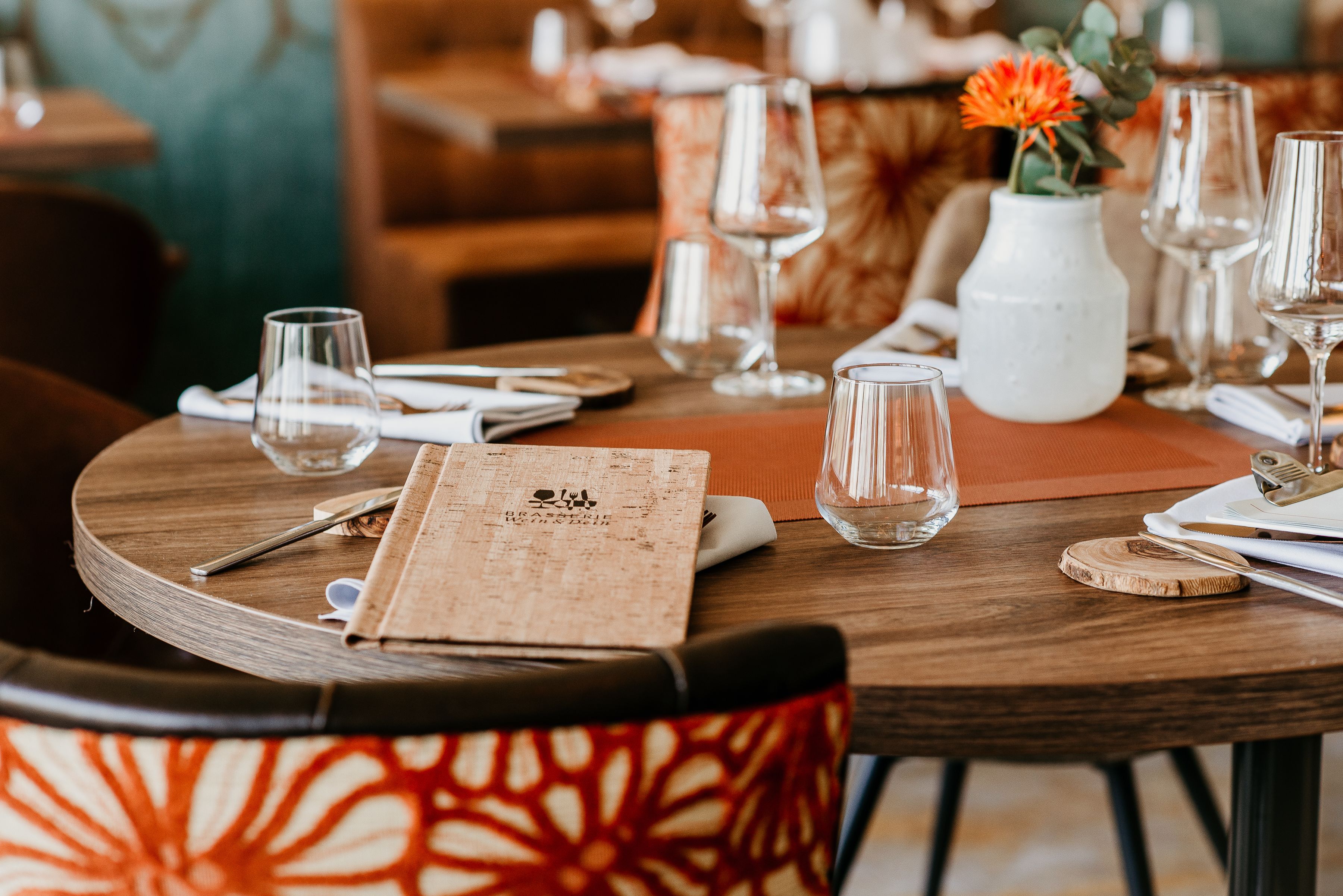 A dining table set with wine glasses, a menu, and a vase with flowers.
