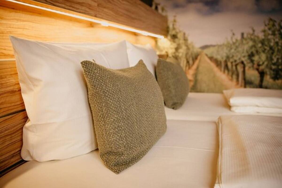 A bed with white and textured pillows, a wooden headboard, and a view of trees in the background.