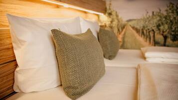 Una cama con almohadas blancas y texturizadas, cabecera de madera y vista a árboles al fondo.
