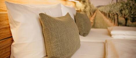 Una cama con almohadas blancas y texturizadas, cabecera de madera y vista a árboles al fondo.