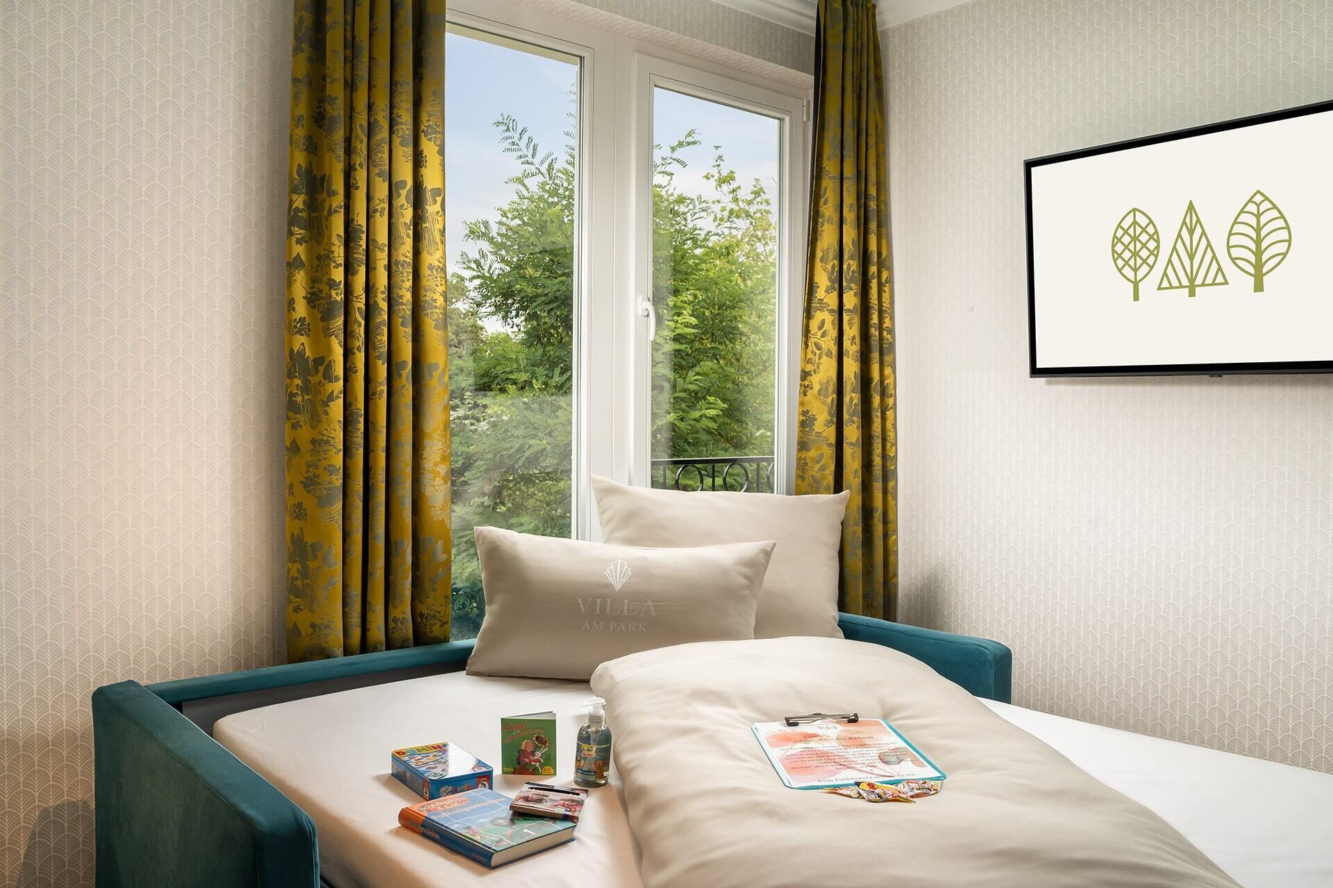 Una camera d'hotel con un letto, una finestra con tende e un quadro appeso al muro, con vista sugli alberi.