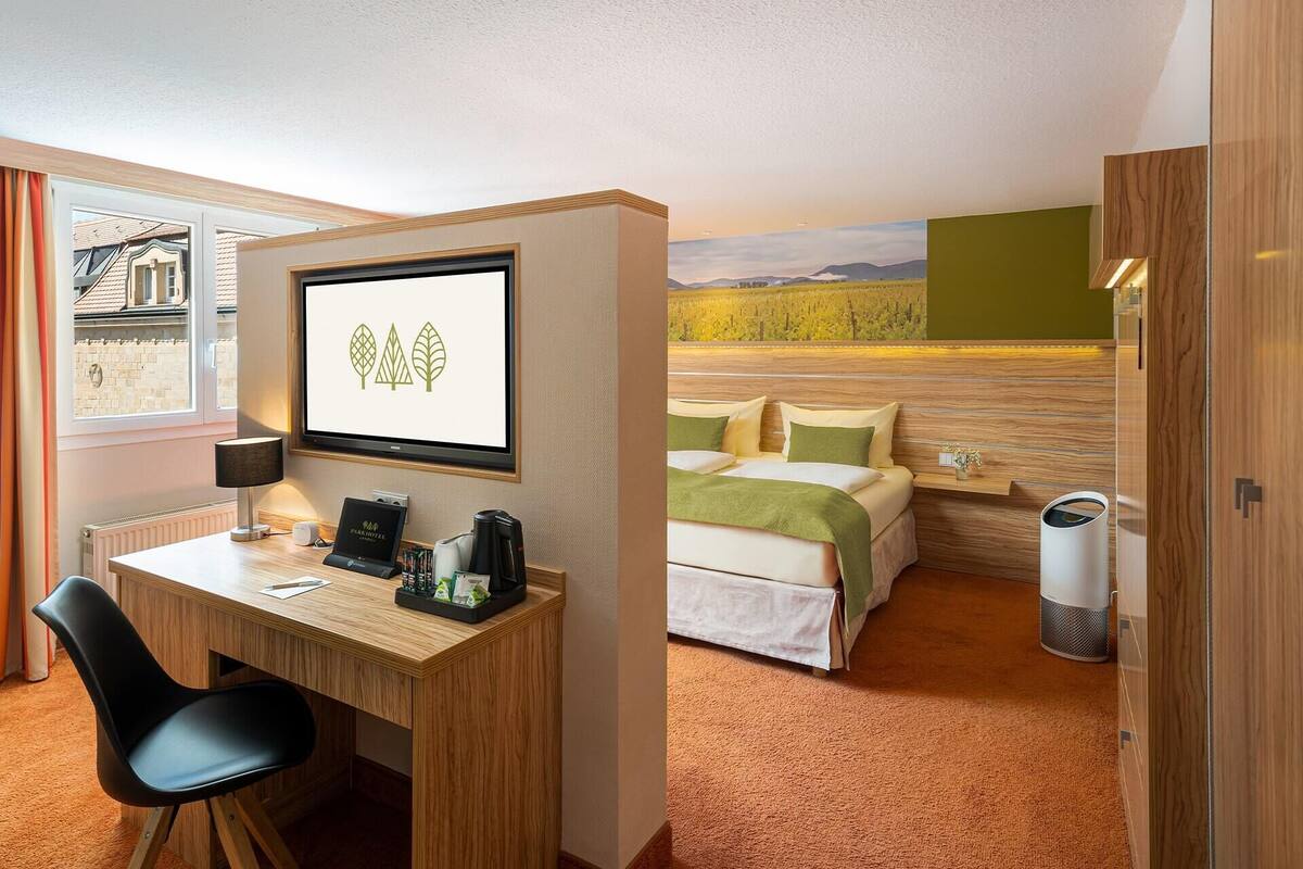A hotel room with a desk, chair, bed, and a view of a vineyard.